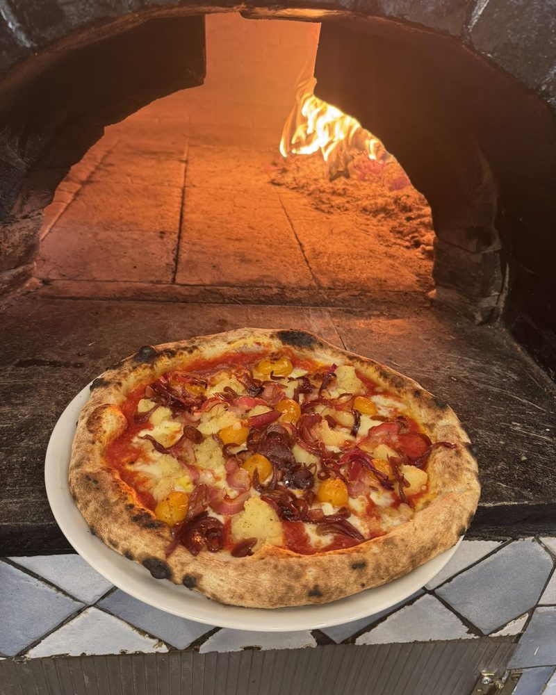 Una pizza appena sfornata davanti alla bocca del forno